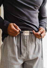 Pantalones de pijama a rayas grises con cintura de cordón, combinados con una parte superior oscura de manga larga. La textura parece suave y la tela se ve liviana.