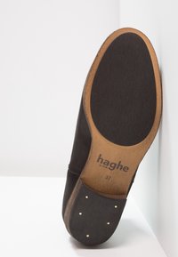 Sohle eines schwarzen Lederschuhs mit Holzabsatz und Metallnägeln, schwarzem Gummi-Griff und "haghe 37" Branding auf der hellbraunen Sohle.