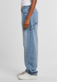 Světle modré džíny z denimu s volným střihem, vysokým pasem a bočními kapsami. Kombinovány s bílými teniskami, které ukazují neformální styl.