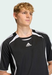 Czarna koszulka sportowa z pionowymi paskami, białymi akcentami i logo Adidas na piersi. Krótkie rękawy i okrągły dekolt.