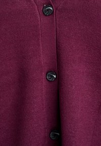 Detailní záběr na burgundskou pleteninu s vertikálním řádkem tří černých kulatých knoflíků přišitých uprostřed.