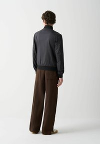 Jachetă bomber neagră cu manșete și guler riblicate, având mâneci texturate și asortată cu pantaloni largi maro. Design minimalist.