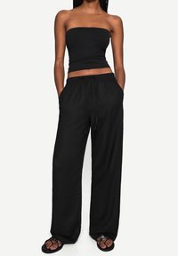 Black strapless top paired with loose black pants. The pants feature an elastic waistband and side pockets. Worn with black flip-flops.