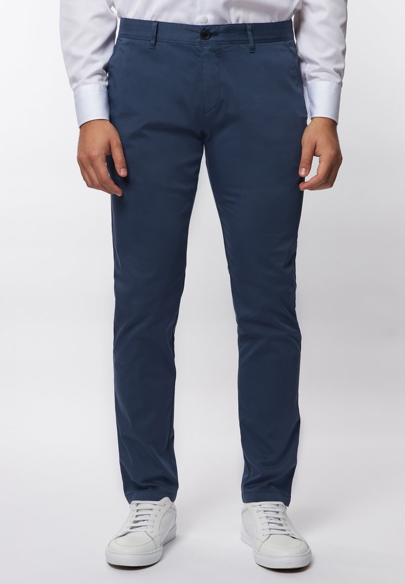 Marineblaue, schlanke Chinos aus glattem Baumwollstoff mit einem Knopfverschluss und frontalen Taschen, kombiniert mit weißen Turnschuhen.