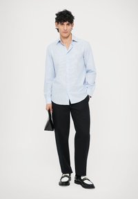 Lys blå stripete skjorte med knappnedkrage, svarte bukser og svarte og hvite sko. Holder en svart clutchveske.