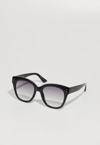 Óculos de sol oversized pretos com lentes escuras em degradê, armação quadrada, acabamento brilhante e tachas douradas nos cantos da armação.
