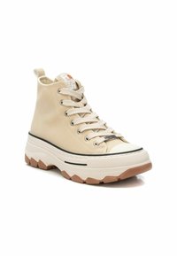 Zapatillas altas beiges con parte superior de lona texturada, suela blanca gruesa, línea de acento negra y punta de goma. Cuenta con cordones y una pestaña en la parte trasera.
