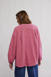 Ροζ ριμπ μακρυμάνικη μπλούζα με στρογγυλή λαιμόκοψη και ακατέργαστες άκρες στις ραφές, σε συνδυασμό με μπλε παντελόνι με λεπτές ρίγες, εμφανιζόμενο από πίσω.