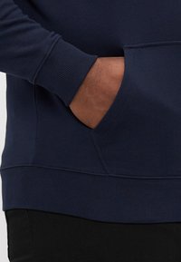 Granatowy sweter z kangurzą kieszenią, ściągaczami przy mankietach i u dołu, wykonany z miękkiej tkaniny bawełnianej z gładką fakturą.