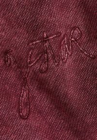 Tessuto bordeaux con una trama testurizzata, caratterizzato da ricami in una tonalità simile, che mette in risalto una superficie morbida e liscia.