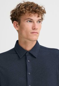 Marineblå polo skjorte med knappelukking, med krage, stoffstruktur og subtile sømmer detaljer.