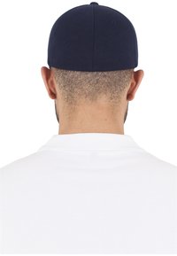Căciulă de baseball bleumarin văzută din spate, având un design structurat și șase panouri. Pur și simplu cu o cămașă polo albă, cu țesătură vizibilă.