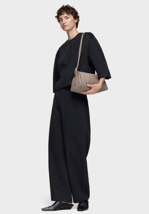 Top negro de lana de gran tamaño, pantalones negros sueltos y zapatos negros de cuña sin cordones. La modelo sostiene un bolso beige texturizado con correa para el hombro.