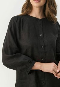 Czarna lniana koszula z okrągłym dekoltem, długimi bufkami i zapięciem na guziki. Posiada subtelną fakturę i małe czarne guziki.