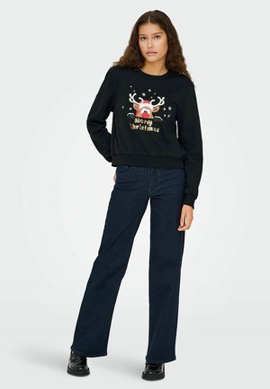 Sudadera negra con gráfico de reno y texto "Feliz Navidad", combinada con vaqueros de pierna ancha azul oscuro y calzado negro.