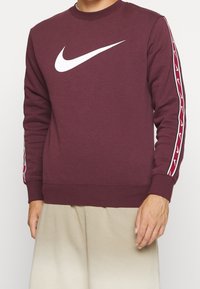 Maroon Nike sweatshirt with a white logo on the front, featuring white and red logo stripes down the sleeves. Soft, textured fabric.
