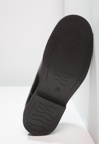 Black sole of a shoe with wave-patterned tread and size number 31 visible, positioned against white background and wall corner.