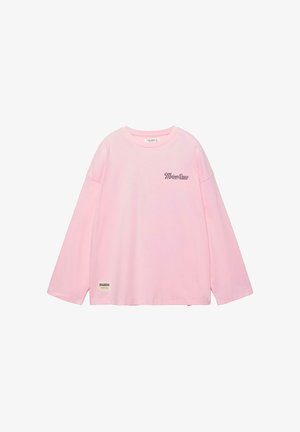 Lyserød langærmet skjorte med teksten "Maison Douce" på brystet og et lille mærke med teksten "Boulangerie" nær den nederste kant.