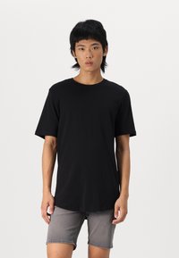 Schwarzes Baumwoll-T-Shirt mit Rundhalsausschnitt und kurzen Ärmeln, das eine leicht verlängerte Form und ein minimalistisches Design aufweist.