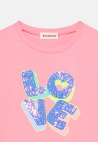 Ροζ βαμβακερό μπλουζάκι με πολύχρωμο γραφικό "LOVE" με υφή από παγιέτες και λεπτομέρεια σε σχήμα καρδιάς μέσα στο γράμμα "O".