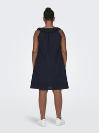 Robe sans manches bleu marine avec un col à volants, comportant des détails brodés au niveau de l'ourlet, dans une forme A-line décontractée. Portée avec des baskets blanches.