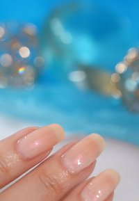 Neutrale nagellak op verzorgde vingers, die een glanzende, gladde afwerking toont met een zachte, doorzichtige nude kleur. Vervaagde blauwe achtergrond.