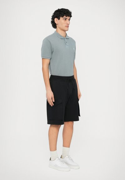 Γκρι πόλο πουκάμισο με κοντά μανίκια, μαύρα σορτς με κορδόνι και πλαϊνές τσέπες, και άσπρα αθλητικά παπούτσια με ανοιχτόχρωμες κάλτσες.