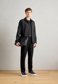 Black wool blend jacket with button closure, paired with a black t-shirt and relaxed black trousers. Accessories include a leather bag and navy sneakers.