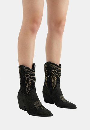 Bottes de cowboy noires avec une finition texturée, ornées de broderies dorées, à bouts pointus et à talon bas empilé. Glissière latérale pour un enfilage facile.
