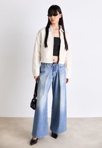 Crème gekort jasje, zwart gecropte top, wijde blauwe denim jeans, zwarte puntige ballerina's, met een kleine zwarte handtas; gladde texturen opgemerkt.