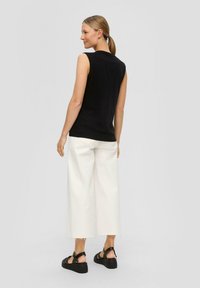 Black sleeveless top paired with wide white cropped pants, and black platform sandals. The outfit features a relaxed fit and minimal design.