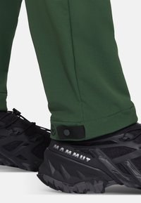 Groene outdoorbroek met een strak ontwerp, voorzien van een veilige sluiting aan de pijpen, gecombineerd met zwarte Mammut wandelschoenen met gestructureerde zolen.