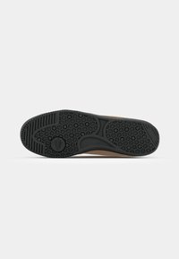 Suela de goma negra con un patrón hexagonal, que presenta un diseño redondeado y una entresuela suave que transiciona a un material color marrón claro.
