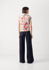 Blommönstrad ärmlös väst i krämfärg med röda och blå blommor, ihopparad med hög midja och mörka denimbyxor med vida ben.