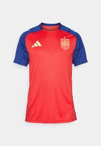 Červený a modrý krátký rukáv dres s kulatým výstřihem, obsahující logo španělské národní reprezentace a tři bílé pruhy Adidas na ramenou.