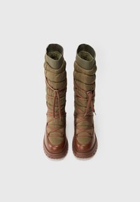Μποτάκια σε ελαιόχρωμο με επενδεδυμένη υφή, καφέ δερμάτινες λεπτομέρειες, ριμπ μανσέτες και κορδόνια σε σταυρωτό σχέδιο, σχεδιασμένα με χοντρή σόλα.