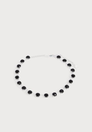 Bracelet avec des pierres noires rondes serties dans des maillons en argent et un fermoir chaîne en argent, présenté sur un fond clair uni.