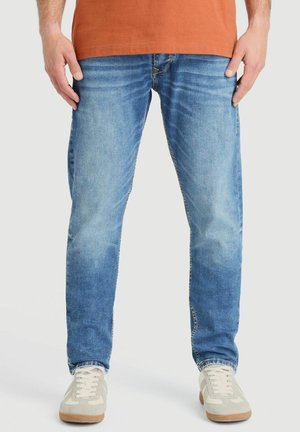Lichtblauwe denim jeans met een rechte pijp, een lichte vervaging en contrasterende stiksels. Gecombineerd met beige sneakers en een roestkleurig shirt.