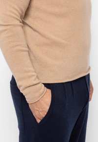 Beiger, gestrickter Pullover mit langen Ärmeln, kombiniert mit marineblauen, strukturierten Hosen mit seitlichen Taschen. Der Schnitt ist leger und lässig.