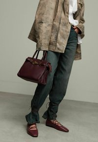 Bordeaux lederen handtas met dubbele handvaten, gouden beslag en ritssluiting. Gemaakt in combinatie met losse denim broek en bijpassende bordeaux schoenen.