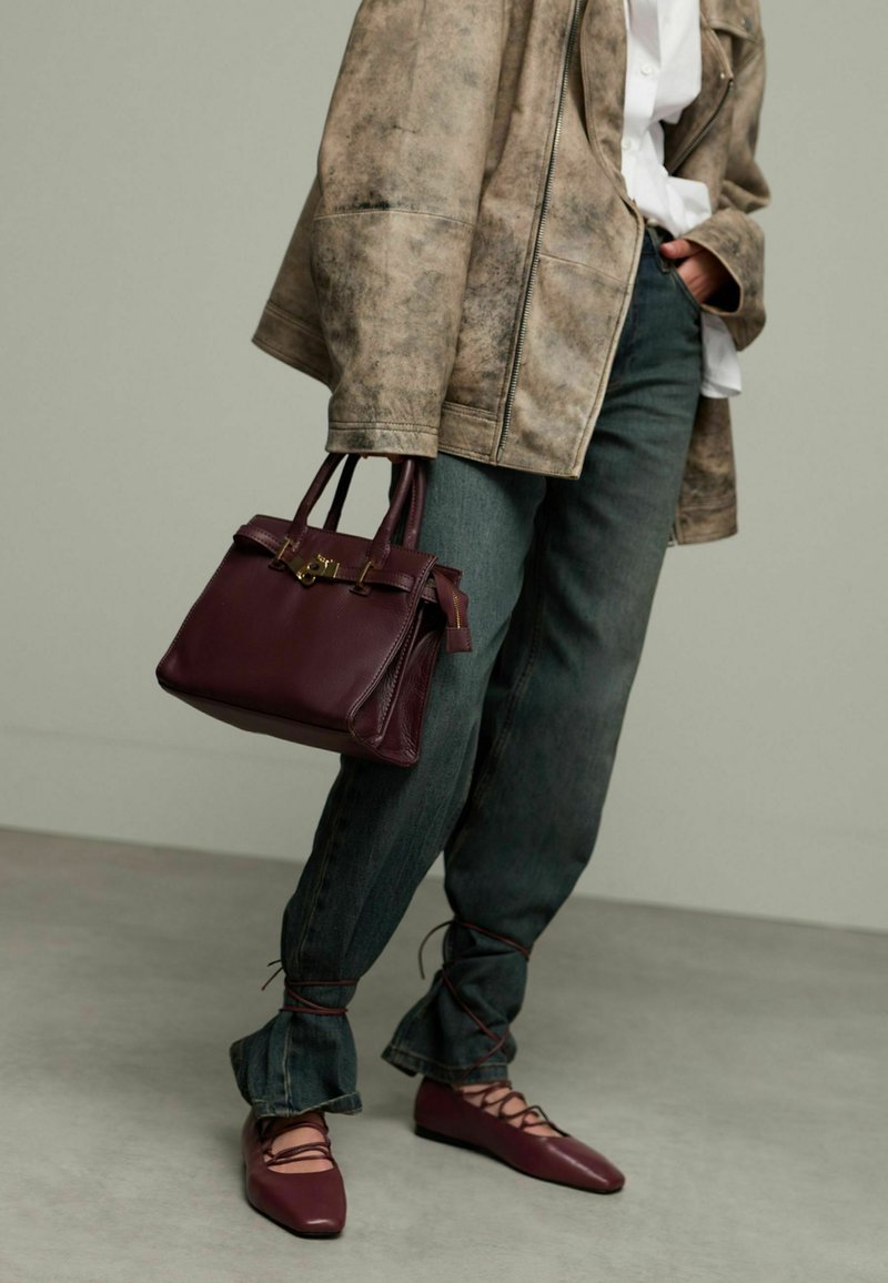 Bordeaux lederen handtas met dubbele handvaten, gouden beslag en ritssluiting. Gemaakt in combinatie met losse denim broek en bijpassende bordeaux schoenen.