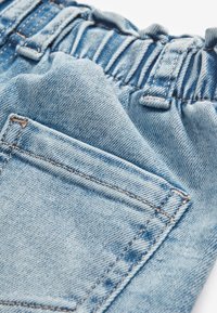 Tissu en denim bleu clair avec une taille élastique et des coutures visibles sur la poche arrière d'un jean.