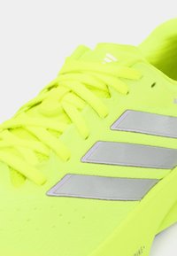 Αθλητικό παπούτσι νέον κίτρινο με υφή στην επάνω επιφάνεια, με ασημί τρεις ρίγες, στρογγυλά κορδόνια και ανατομική σόλα.