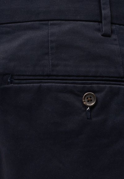 Κοντινή λήψη σε ύφασμα σκούρου ναυτικού με πίσω τσέπη που έχει ένα μόνο κουμπί και ραμμένη θηλιά για ζώνη πάνω από τη ζώνη της μέσης.
