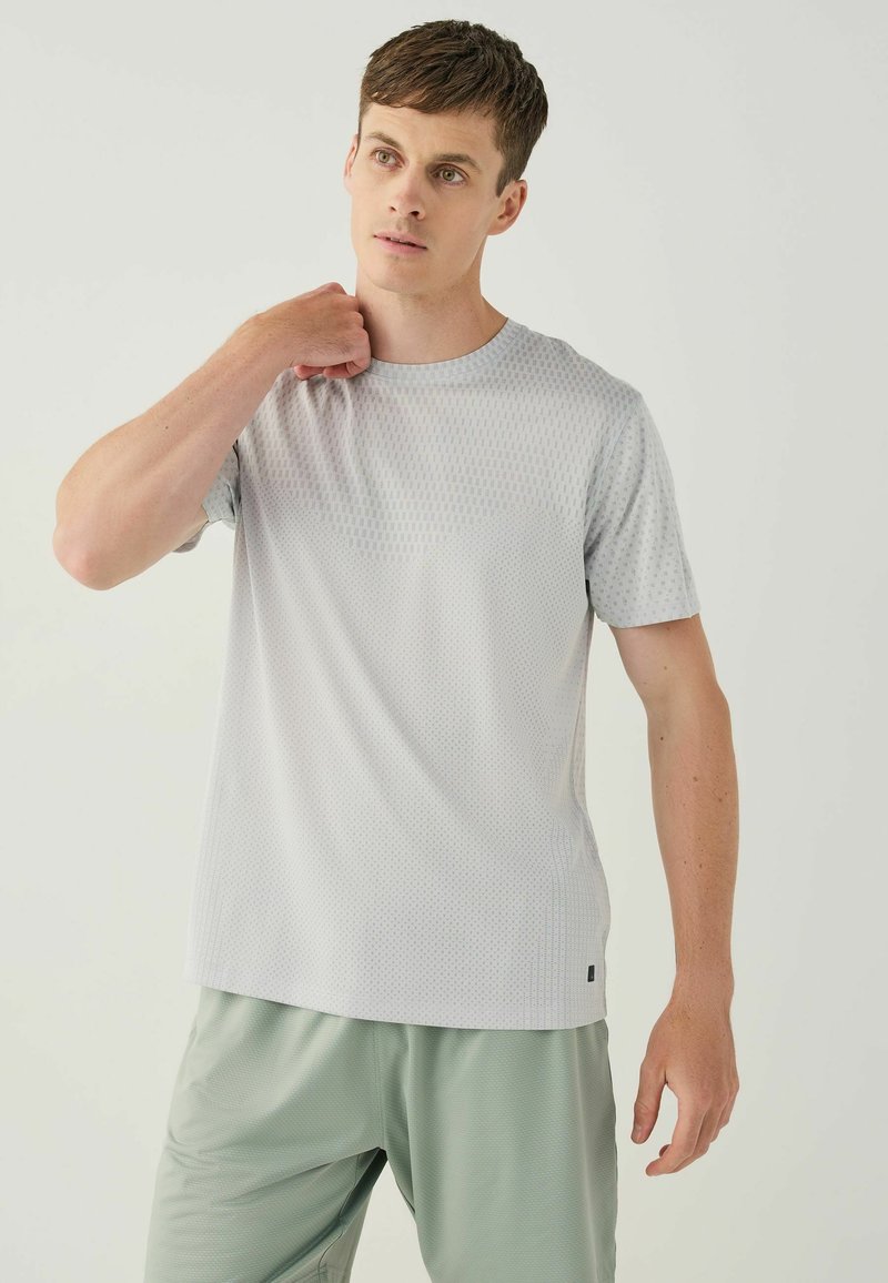 Light gray short-sleeve athletic shirt with a textured pattern, round neckline, and small black logo at the hem. Worn with gray shorts.