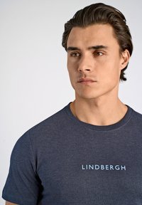 Camiseta de algodón azul marino con el texto "LINDBERGH" en fuente azul clara, cuello redondo y mangas cortas. Textura suave.