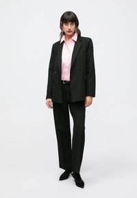 Blazer nero doppiopetto, camicia rosa, pantaloni neri e ballerine appuntite. Tessuto liscio, vestibilità su misura e colori a contrasto.
