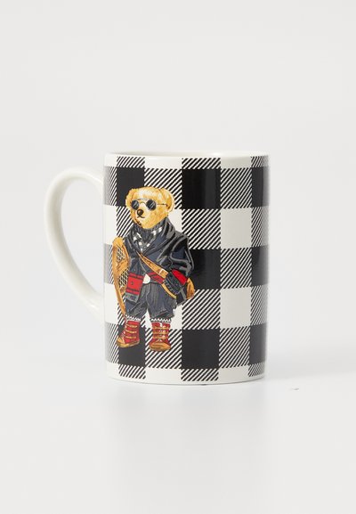 Taza blanca con patrón de cuadros negros que presenta un oso usando gafas de sol, un abrigo, botas y sosteniendo una raqueta de nieve.