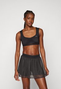 Crni sportski crop top s nabranym detaljem i dizajnom racerback, u kombinaciji s crnom prozirnom suknjom s elastičnim pojasom.