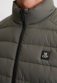 Gepolsterte Jacke in Dunkelgrün mit hohem Kragen und schwarzem Reißverschluss. Auffälliges Logo-Patch mit "MOP" in Cremefarben auf der Brust.